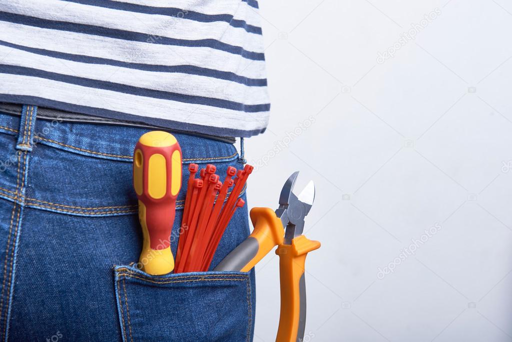 Tools for electrician in back pocket of blue jeans worn by a woman. Screwdriver, cutters and zip ties.