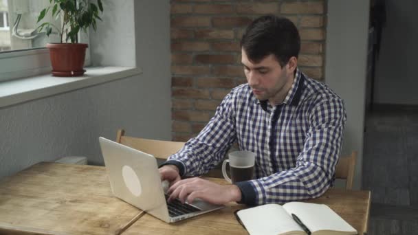 Un uomo con una camicia a quadri, fissa il monitor, beve un sorso di caffè . — Video Stock