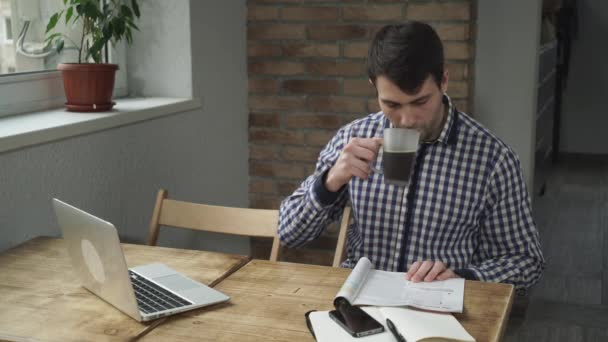 Dans le café l'homme assis à une table lisant un magazine et buvant du café . — Video