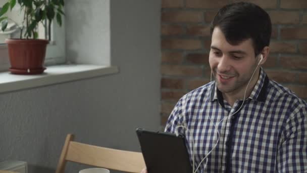 Un hombre sosteniendo una tableta en los oídos auriculares, bienvenida compañero en línea . — Vídeos de Stock