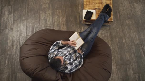 El hombre con el libro en la mano sentado en una silla. Vista desde arriba . — Vídeos de Stock