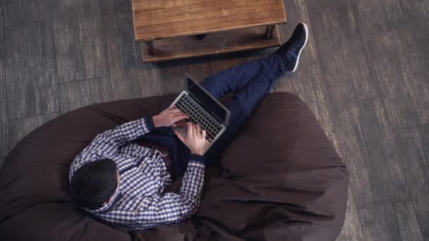 Homem deitado em uma poltrona, segurando um laptop e digitando . — Vídeo de Stock