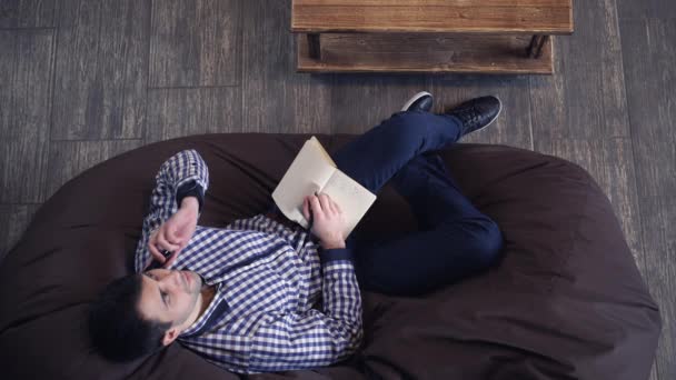 Homem atraente falando ao telefone enquanto estava deitado em uma cadeira . — Vídeo de Stock