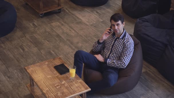 Atraktivní muž sedí a mluví po telefonu na stolní desku, muž s úsměvem. — Stock video