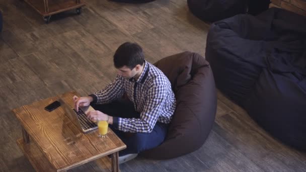 Менеджер сидить у коворкінгу і працює на ноутбук на столі апельсиновий сік . — стокове відео