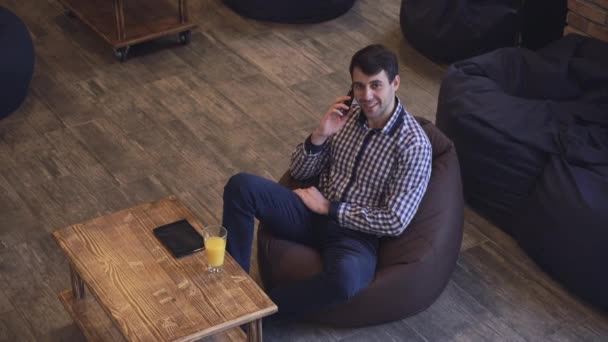 Usmívající se muž mluví na telefon, pomerančový džus a desky na stůl. — Stock video