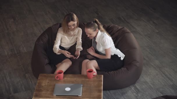 Due donne d'affari attraenti che si rilassano su un divano e guardano foto al telefono — Video Stock