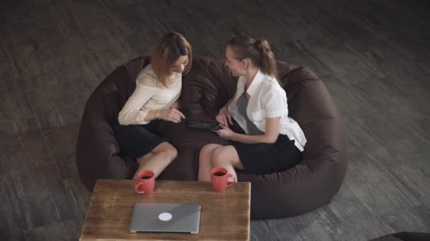 Två attraktiva affärskvinna koppla av på en soffa och tittar på bilden på tabletten. — Stockvideo