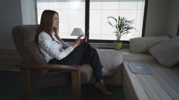 Gelukkig zakenvrouw zittend op de fauteuil met een tablet heeft een pauze — Stockvideo