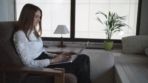 Typy kobieta na laptopie w pobliżu duże okna w domu — Wideo stockowe