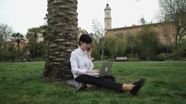 Mujer en el parque trabajando en hierba bajo el árbol — Vídeos de Stock