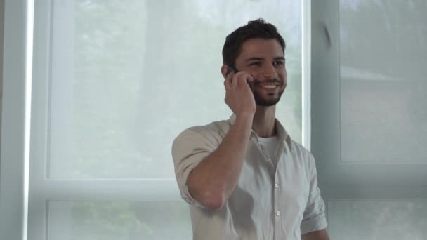 Joven hombre de negocios hablando en el smartphone cerca de la ventana . — Vídeos de Stock
