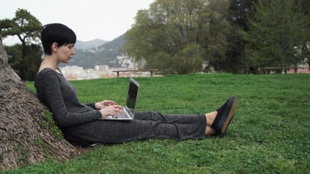 Jeune femme assise sous l'arbre avec ordinateur portable . — Video