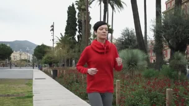 Jeune femme courant dans le parc avec des palmiers des arbustes et des fleurs exotiques . — Video