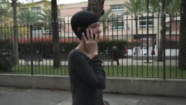 Mujer caminando por el parque infantil hablando en el teléfono inteligente en la ciudad . — Vídeos de Stock