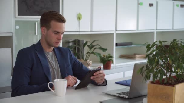 Красивий бізнесмен в сучасному офісі читає пошту на сенсорному планшеті . — стокове відео