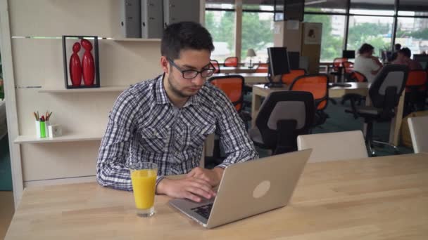 Hombre guapo trabajando con el ordenador portátil y beber jugo de naranja . — Vídeo de stock