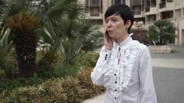 Mujer con pelo corto utilizando la aplicación en el teléfono inteligente al aire libre . — Vídeo de stock