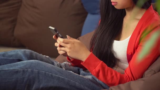 Жінка сидить на кріслі кольорового мішка, друкуючи смс на мобільному телефоні — стокове відео