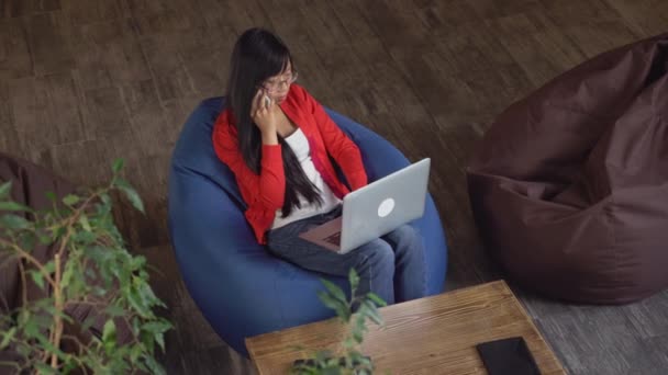 Aziatische meisje typen op laptop en praten op mobiele telefoon. — Stockvideo