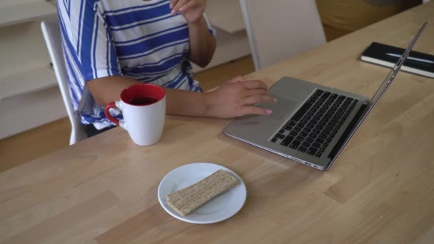 Unerkennbare Frau tippt am Computer und nimmt Snack. — Stockvideo