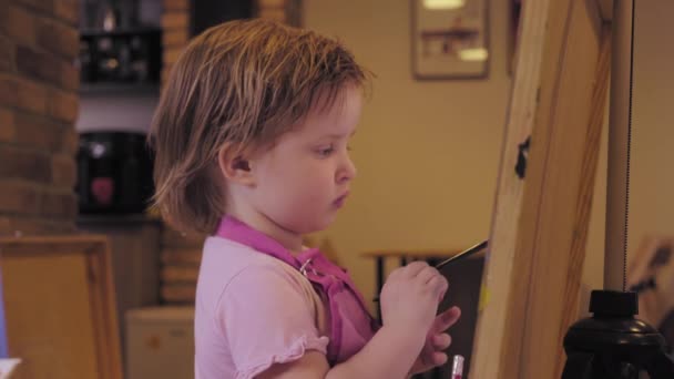 Το κοριτσάκι ζωγραφίζει πάνω σε καμβά στο στούντιο και χαμογελαστός. — Αρχείο Βίντεο