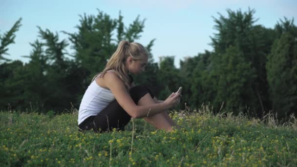 Camicia ragazza si siede su una collina e guadagnando un messaggio sul tuo cellulare . — Video Stock