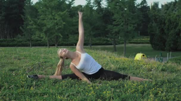Gömlekli ince sarışın genç hill Park yeşil çim ile egzersiz eğilmek gerçekleştirir. — Stok video
