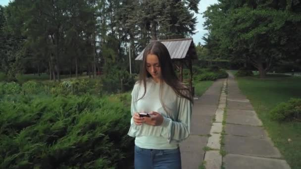 En flicka i en blus går på banan i parken och blir meddelandet. — Stockvideo