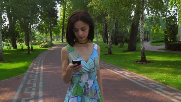 Молодая девушка идет по дорожке в парке и получает сообщение по телефону . — стоковое видео