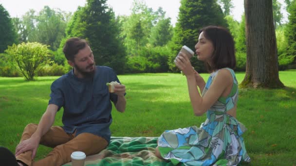 El tipo con la chica come sándwiches de ensalada en el picnic bañado con café. Comunicarse entre sí . — Vídeo de stock