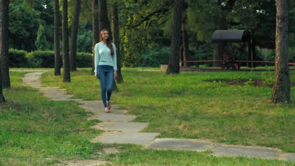 Ung brunett flicka är på väg i en park och blickar upp. — Stockvideo