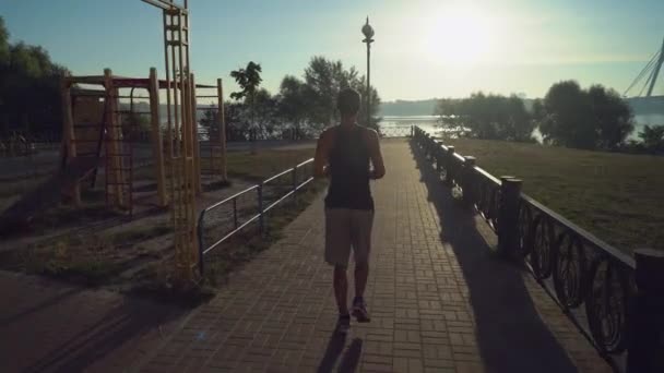 湖の近くのフェンスの道に沿ってカメラを走っている男. — ストック動画