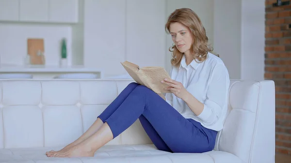 Frau liest auf der Couch sitzend ein Buch lizenzfreie Stockfotos