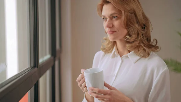 Geschäftsfrau steht mit einer Tasse Kaffee am Fenster Stockbild