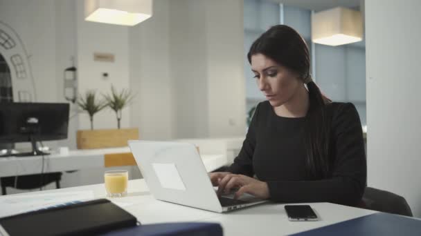 Una mujer que trabaja en la computadora y bebe jugo de naranja — Vídeo de stock