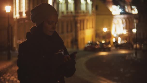 Девушка на вечерней улице, пьет кофе — стоковое видео