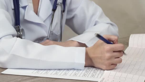 O médico olha cardiograma e faz anotações em um documento . — Vídeo de Stock
