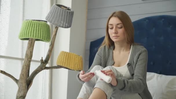 Flickan sitter på sängen gnuggar grädde i benet. — Stockvideo