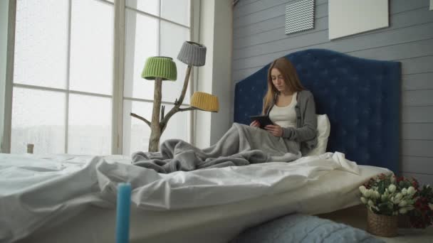 Young girl sitting on a bed with a tablet — Stock Video