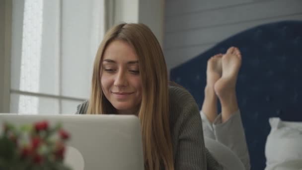 Lächelndes Mädchen mit Laptop im Bett liegend — Stockvideo