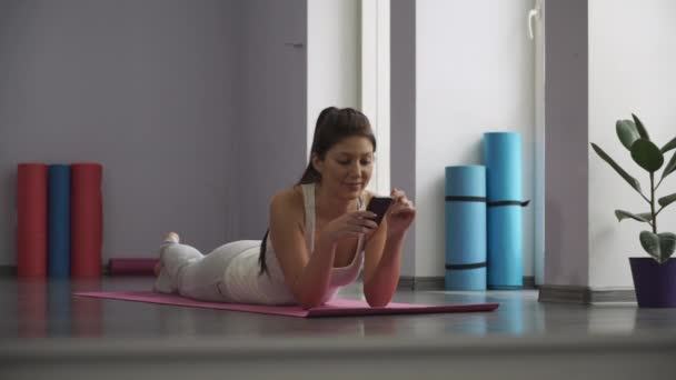 Meisje liggend op de mat van de yoga en kijken naar de telefoon. — Stockvideo
