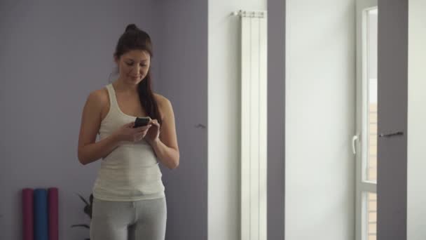 Frau steht mit dem Handy im Fitnessstudio — Stockvideo