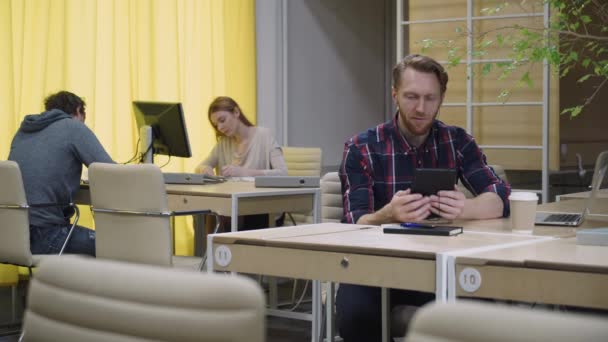 Otwarta przestrzeń ludzi pracy, człowiek w słuchawkach rozmawia z tabletem. — Wideo stockowe