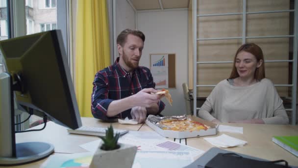 Mann und Frau essen Pizza am Arbeitsplatz. — Stockvideo