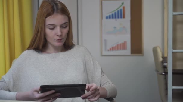 Vrouw zit op de werkplek, in de handen met de tablet. — Stockvideo