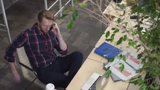 Ein bärtiger Mann sitzt auf einem Stuhl und telefoniert. — Stockvideo