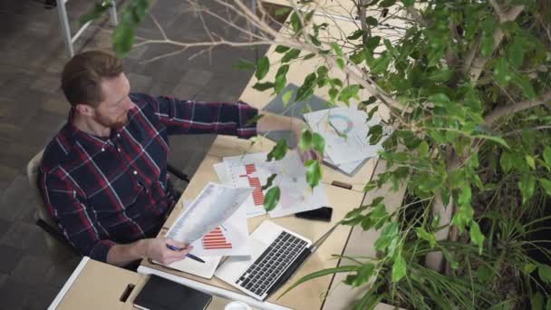 髭の男は環境のオフィスで座っているし、紙の上の数字を見て. — ストック動画
