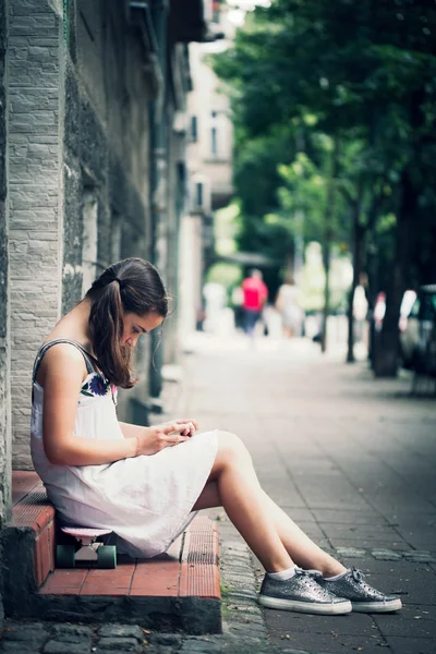 Niña sentarse en el uso de skate smartphone —  Fotos de Stock