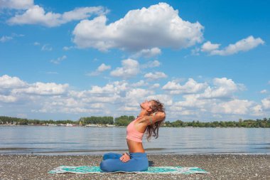 Nehir kıyısında yoga ve nefes alma pratiği yapan genç bir kadın. Güneşli yaz günü sağlıklı yaşam tarzı konsepti.